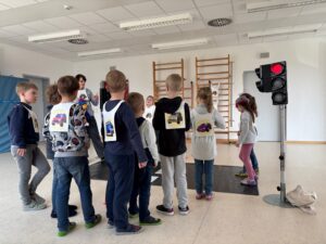 Kinder stehen am Zebrastreifen an einer roten Ampel und hören dem Vortrag zu